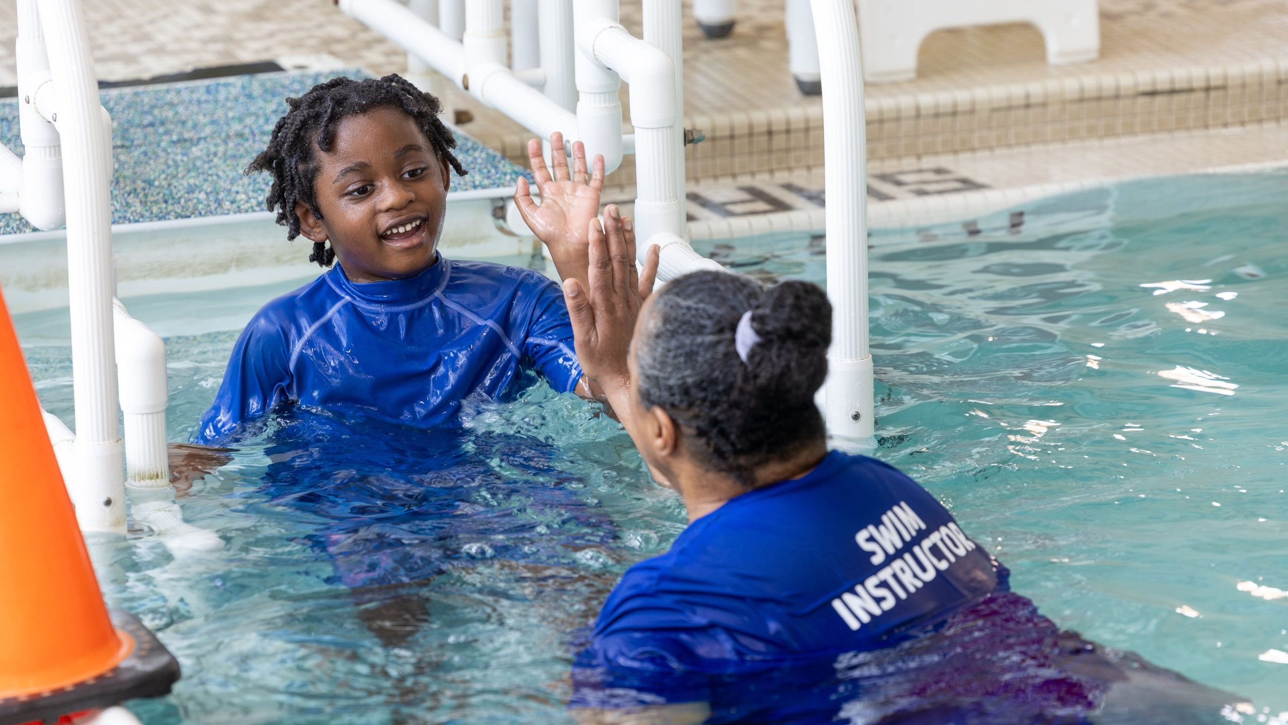 adaptive swim lessons BC - Swim instructor giving high-five to child with disability during adaptive swim lesson