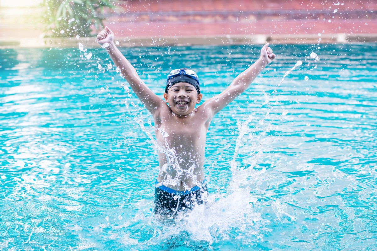 kids swim lessons BC - Excited child splashing in pool during swim lesson