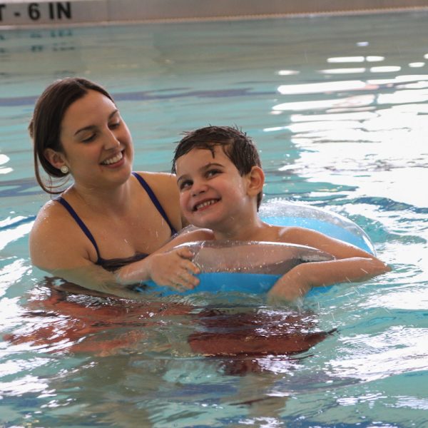 adaptive swim lessons BC - Professional swim instructor providing gentle support to a smiling child with special needs in a warm pool environment